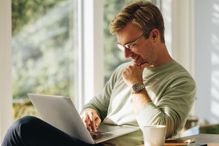 Man in glasses with hand on chin using a laptop on his lap